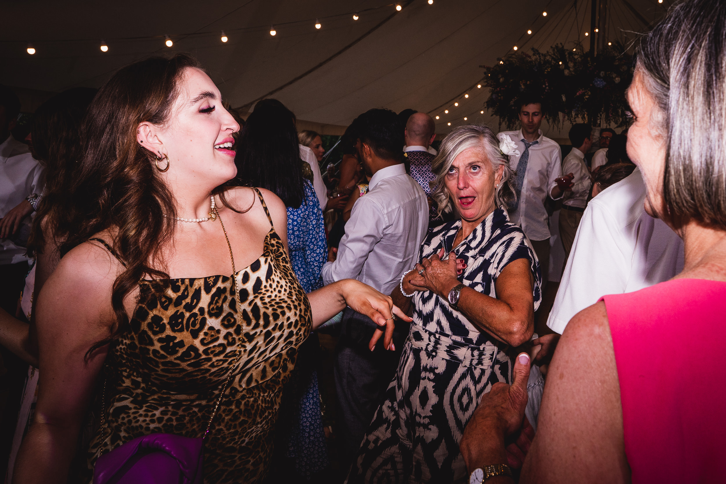 A group of people, including the bride and groom, dancing in a tent at a wedding while being photographed by the wedding photographer.
