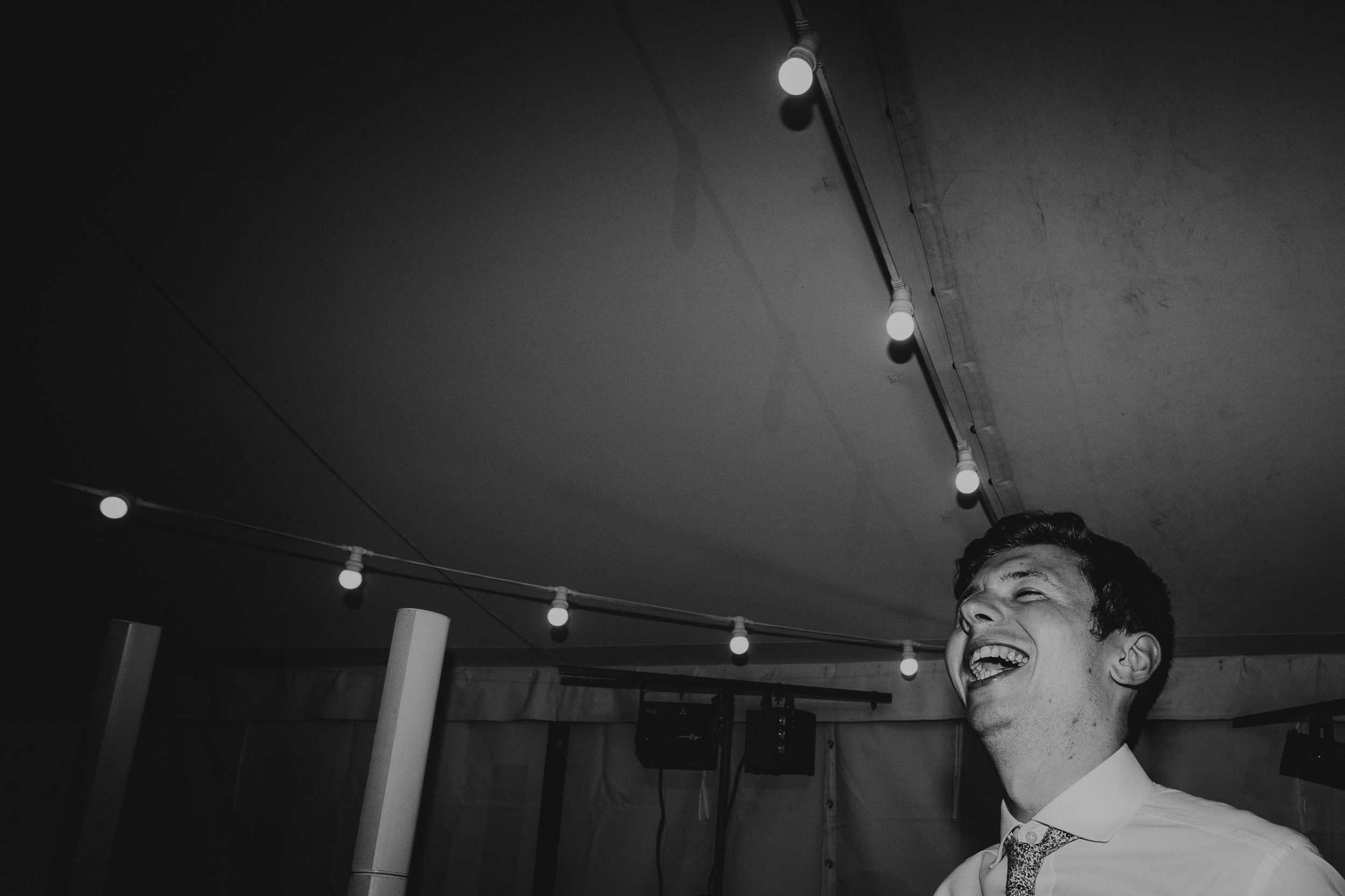 A black and white photo of a man laughing in a tent at a wedding.