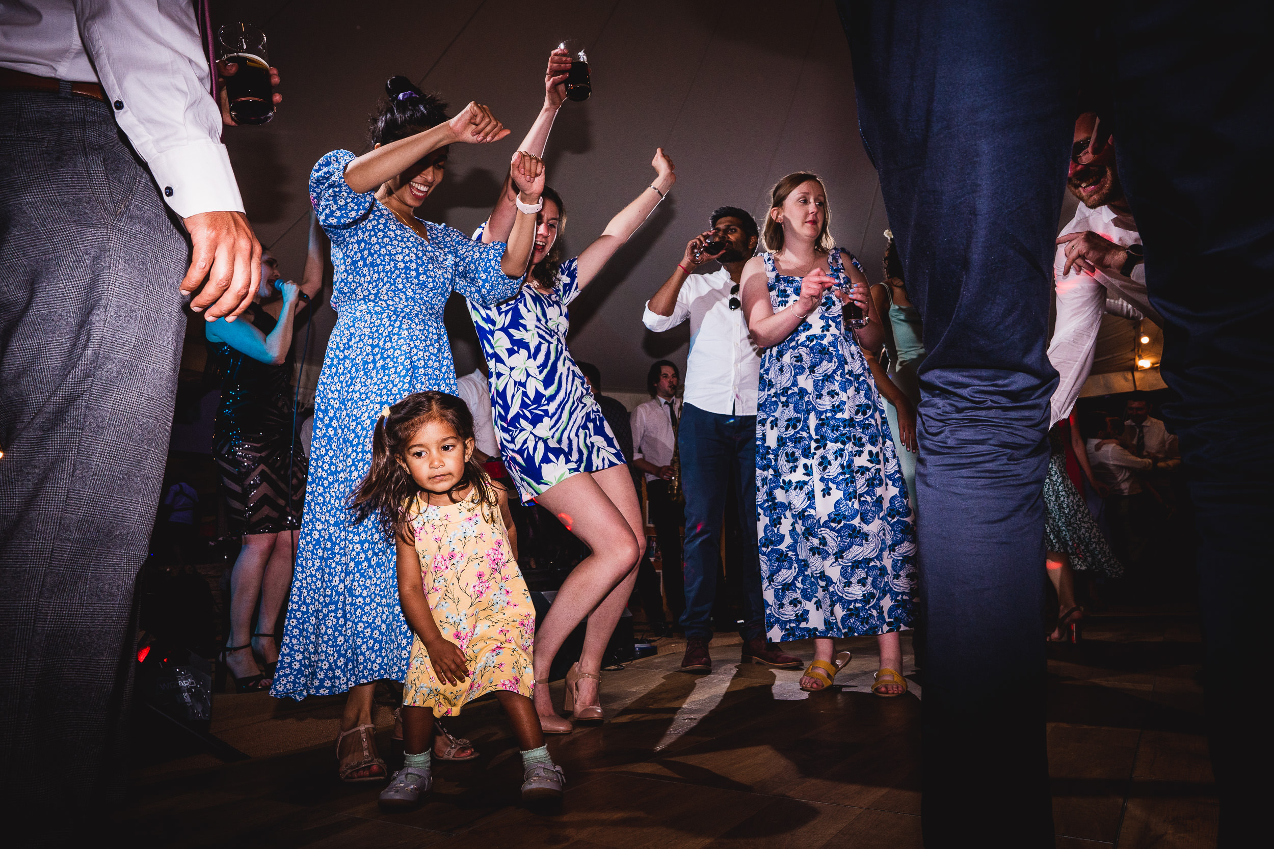 A little girl is dancing on the dance floor at a wedding while the groom and wedding photographer observe.