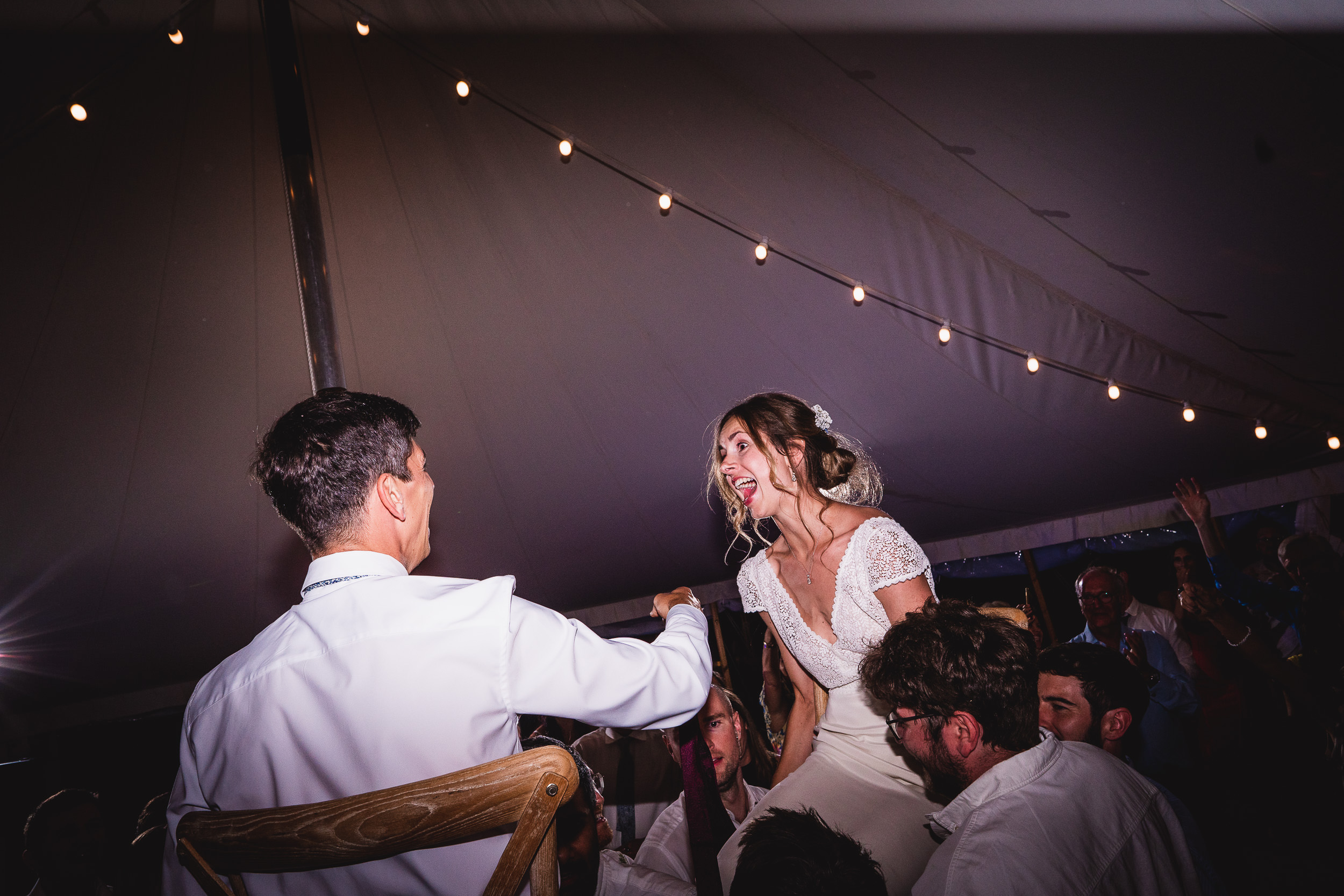 A wedding photographer captures a bride and groom in front of a tent.