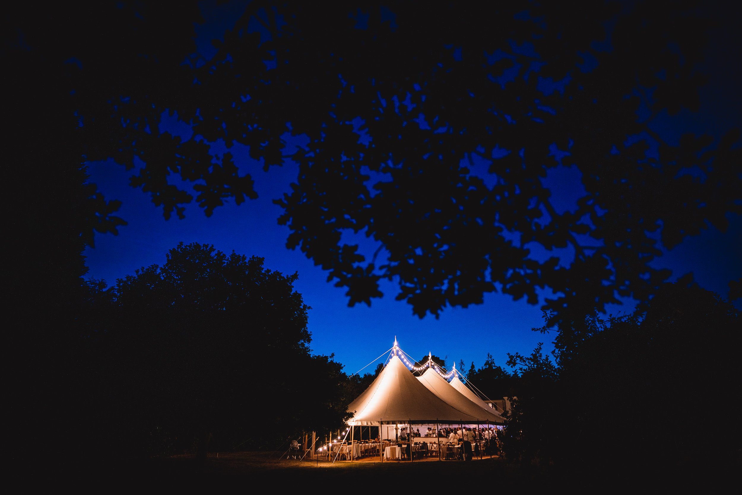 A wedding tent glowing in the nighttime forest, captured by a wedding photographer.