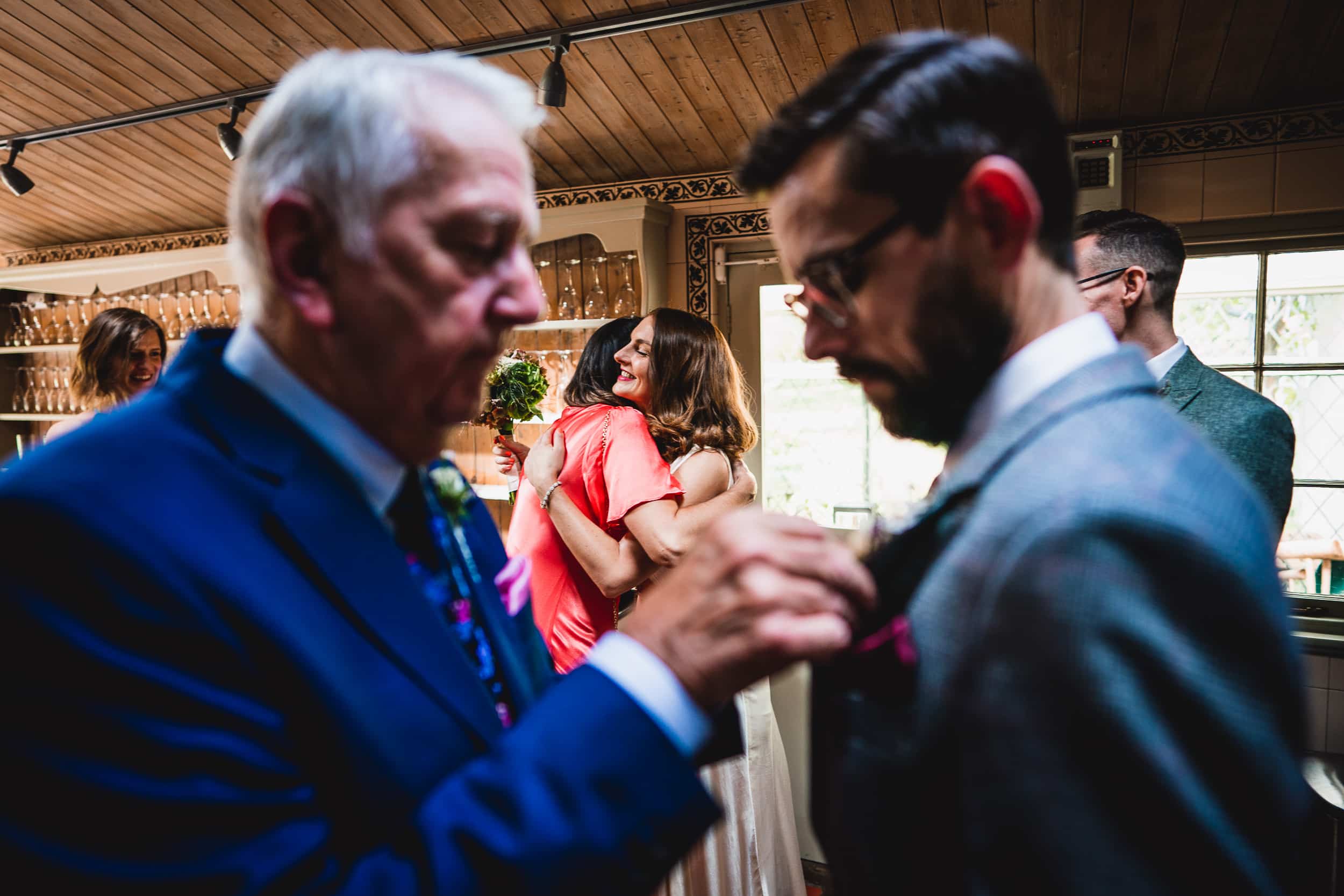 At a Surrey wedding, a man in a suit meticulously adjusts another man's tie at Ridge Farm.