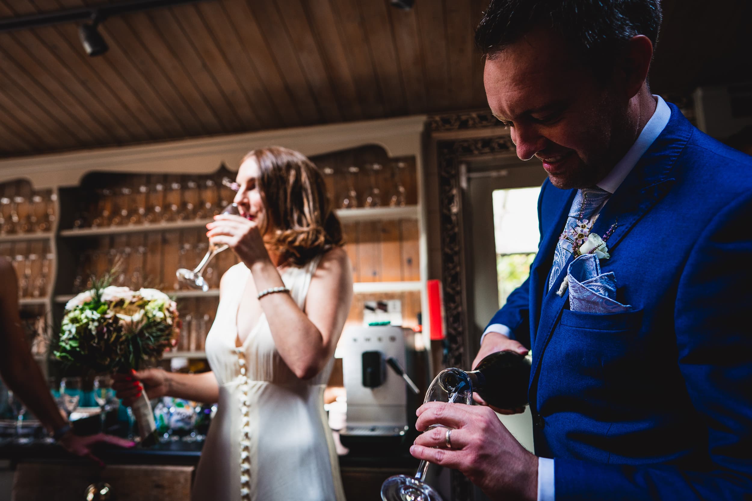 A Surrey wedding at Ridge Farm is captured in this delightful image of a bride and groom pouring wine in a bar.