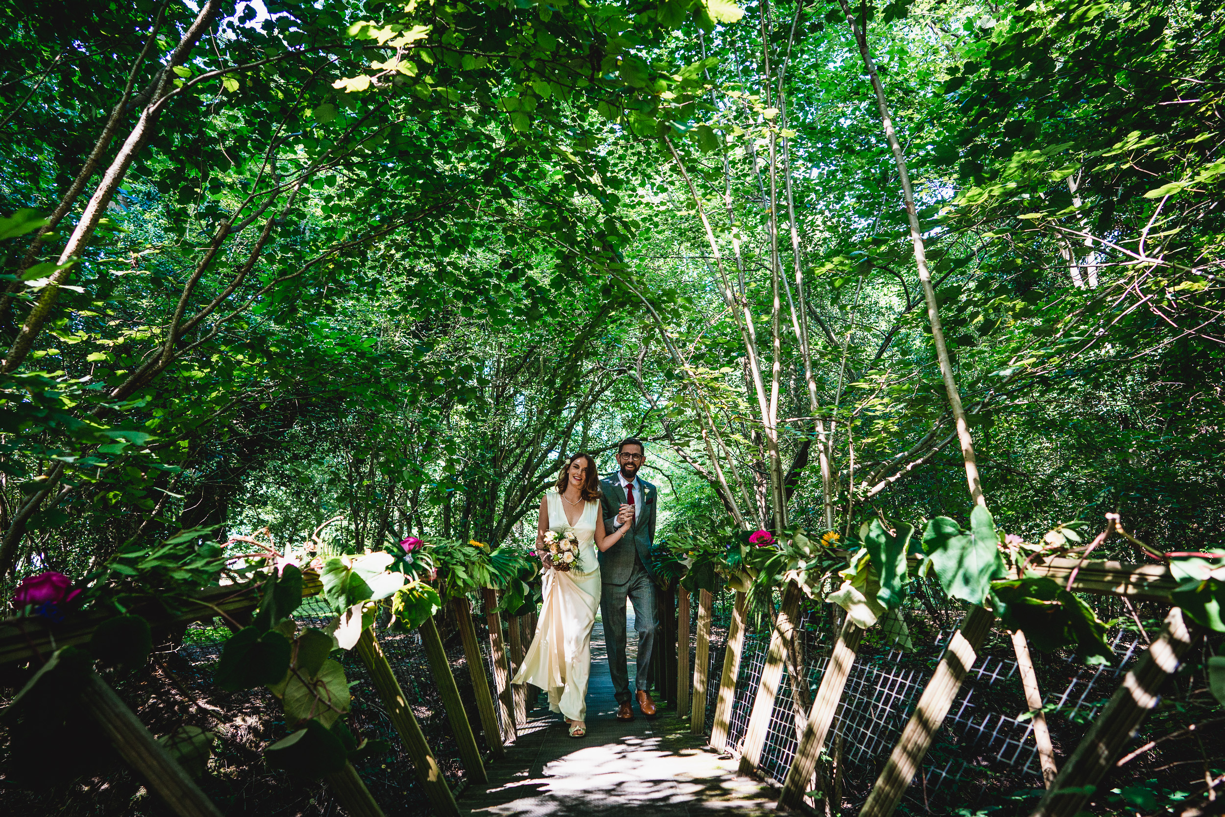 A bride and groom standing on a wooden bridge during their Surrey wedding in the woods at Ridge Farm.