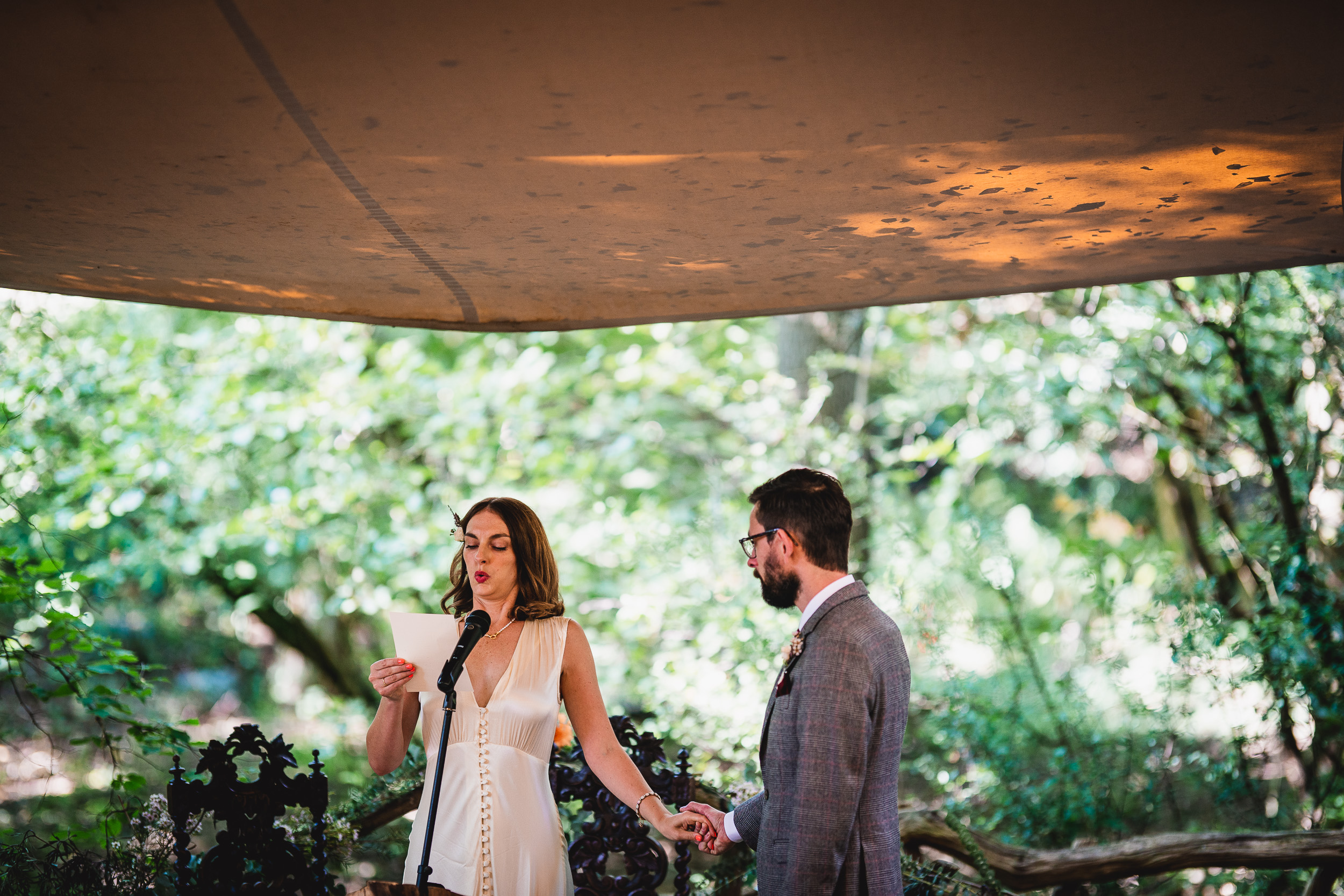 A bride and groom exchange vows under a tent in the Ridge Farm woods, Surrey Wedding.