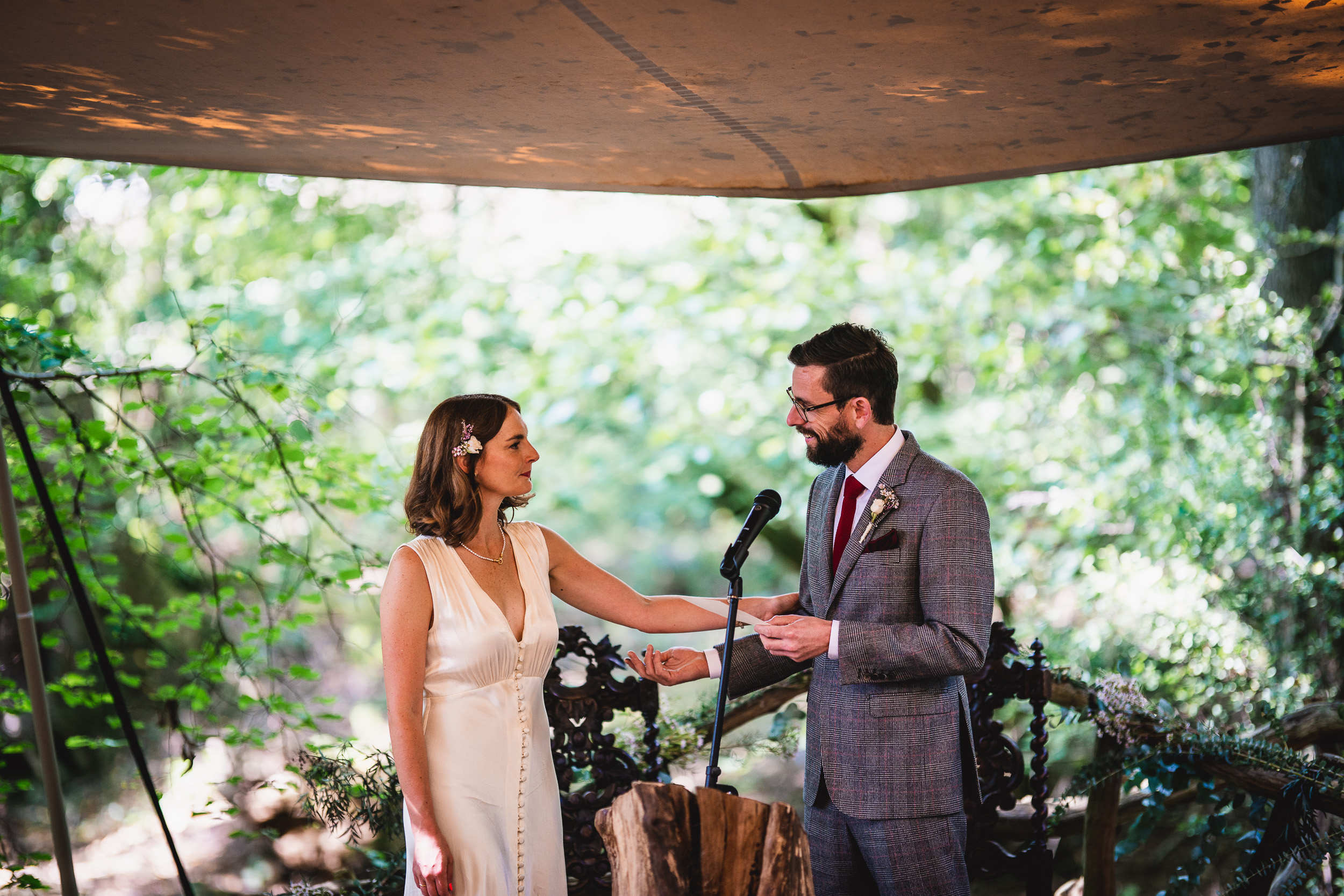 A bride and groom exchange vows at Ridge Farm, a picturesque Surrey wedding venue, under a tent in the enchanting woods.