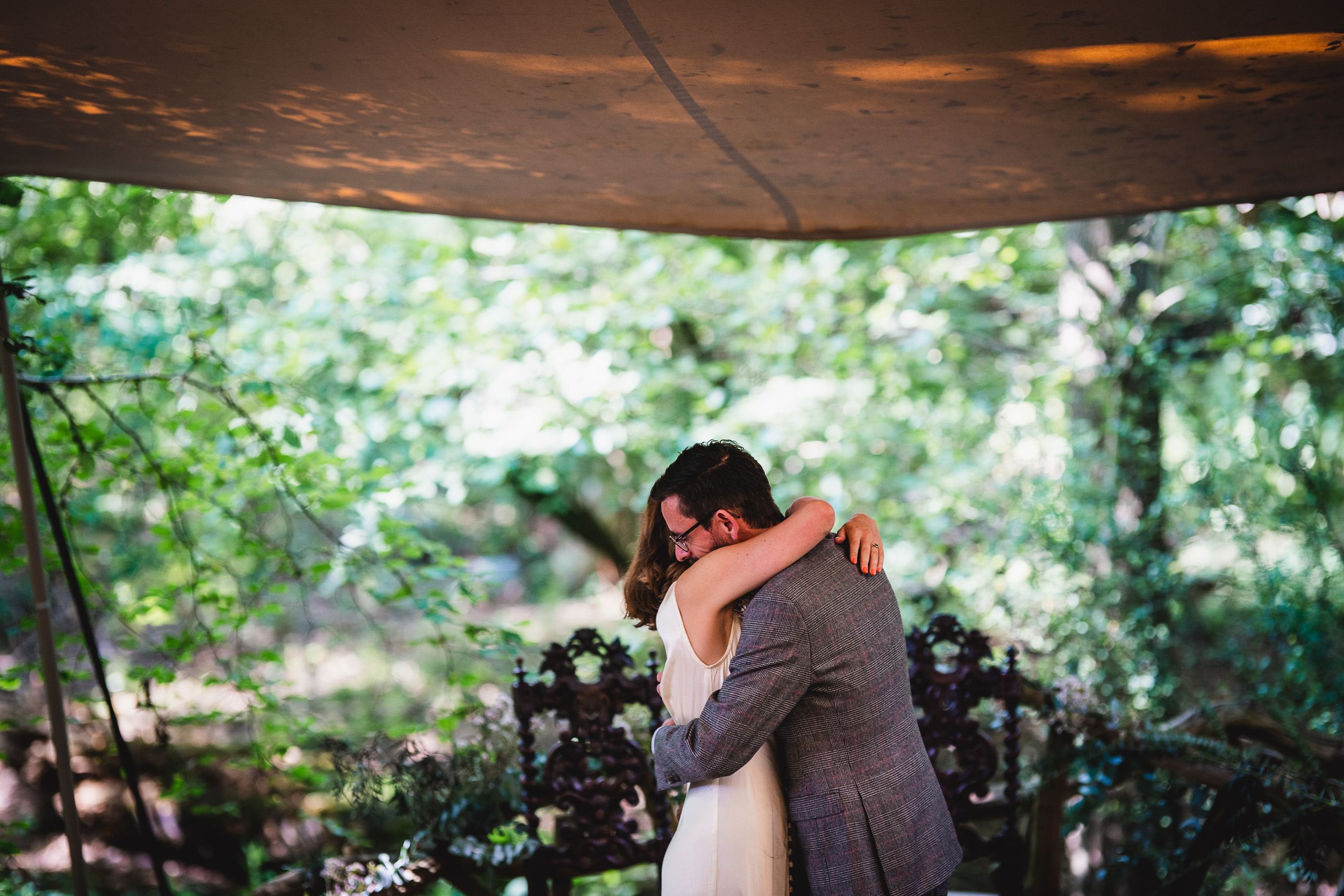 A bride and groom hugging under a tent in the woods at Ridge Farm, Surrey Wedding.