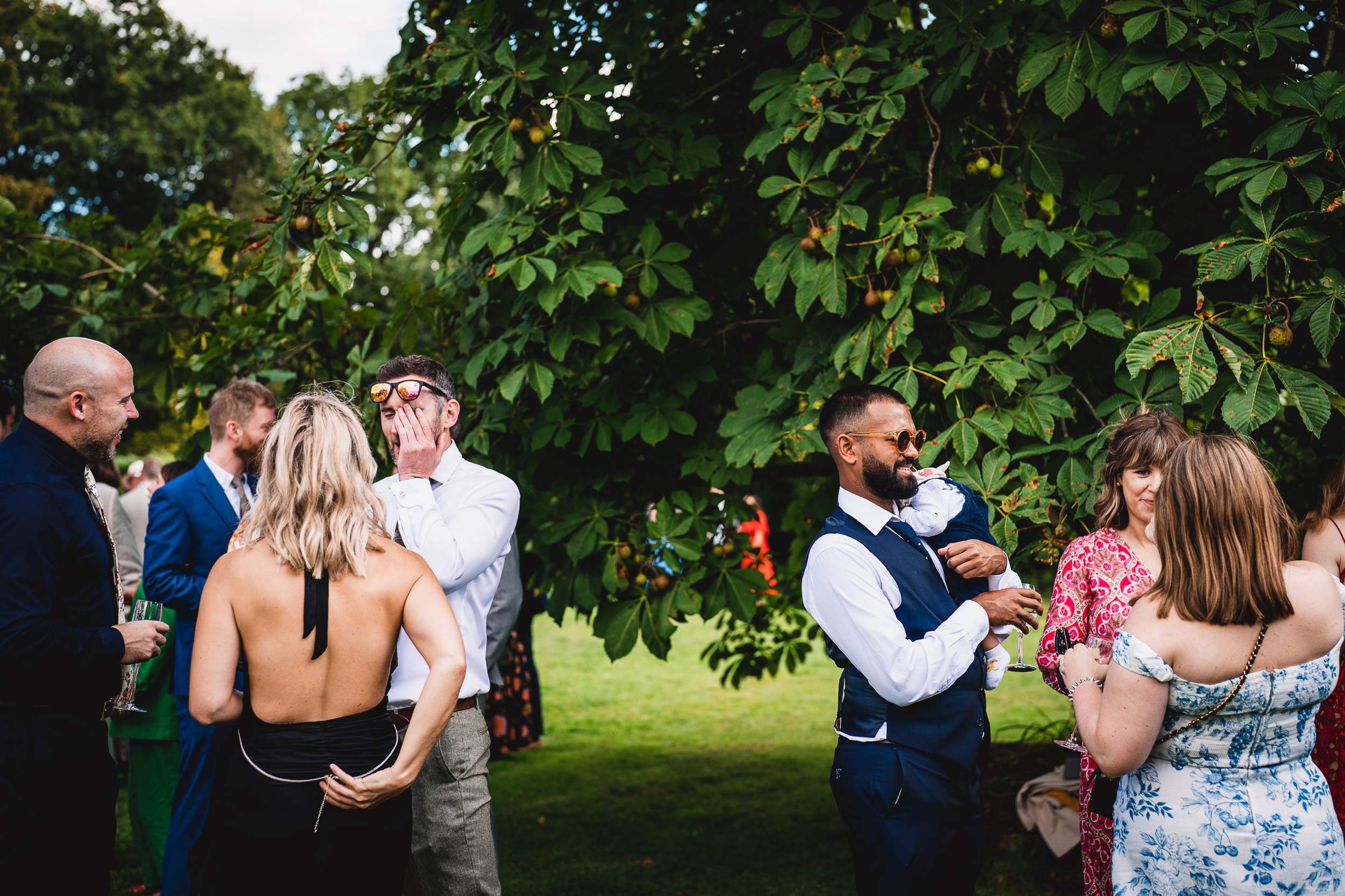A group of Surrey Wedding guests gathered around a tree at Ridge Farm.