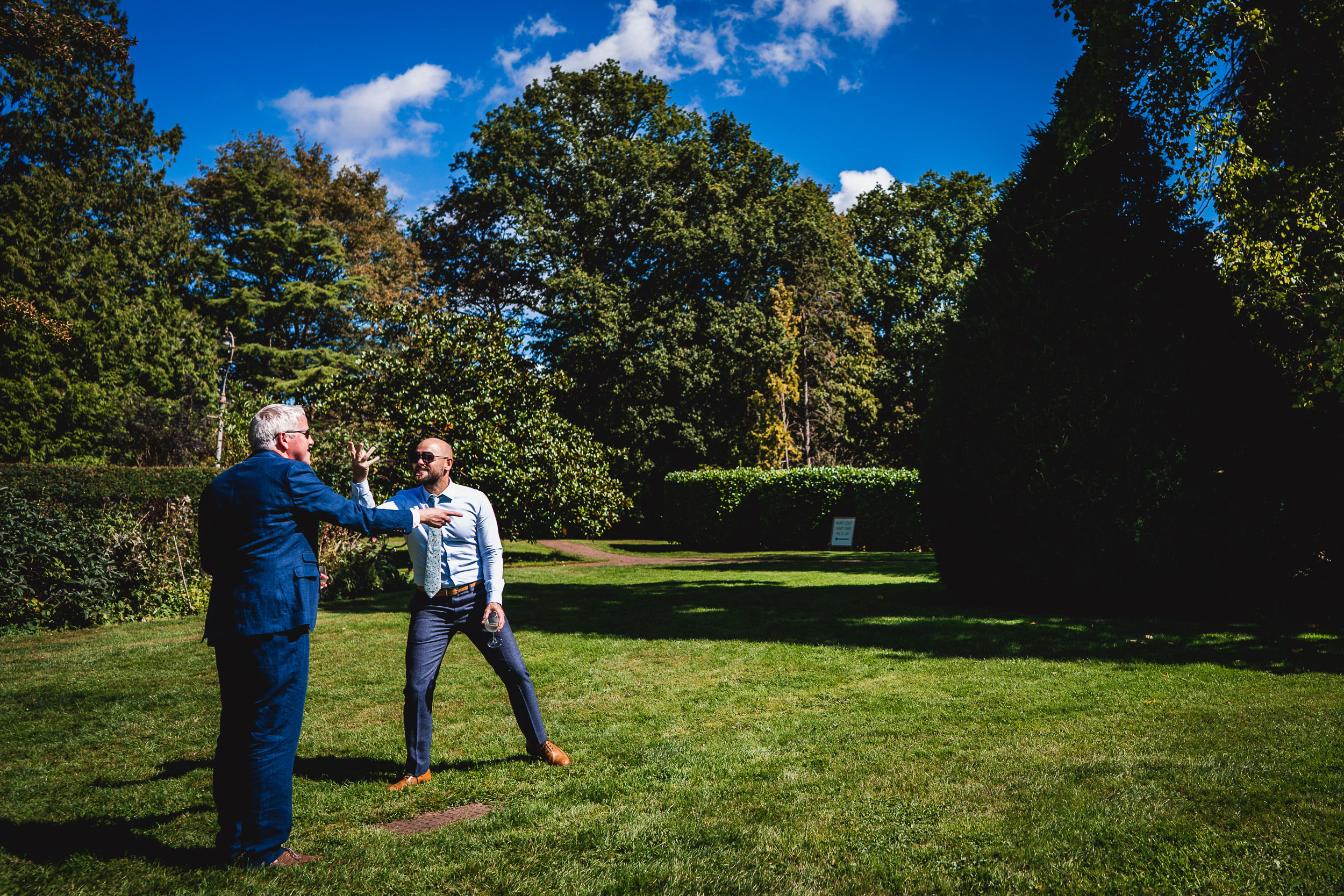 Two men in suits standing in a grassy area at Ridge Farm for a Surrey Wedding.