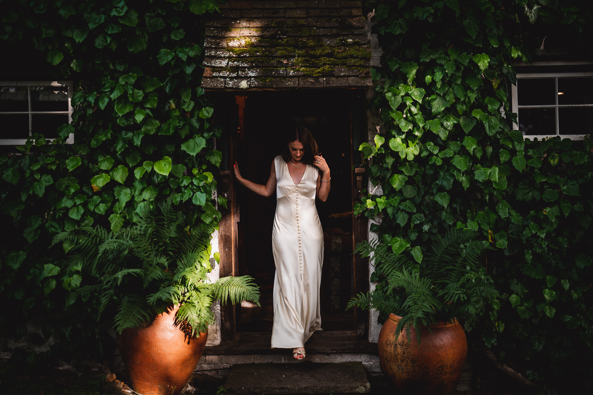 A Surrey bride in a white dress standing in the doorway of Ridge Farm house with ivy.