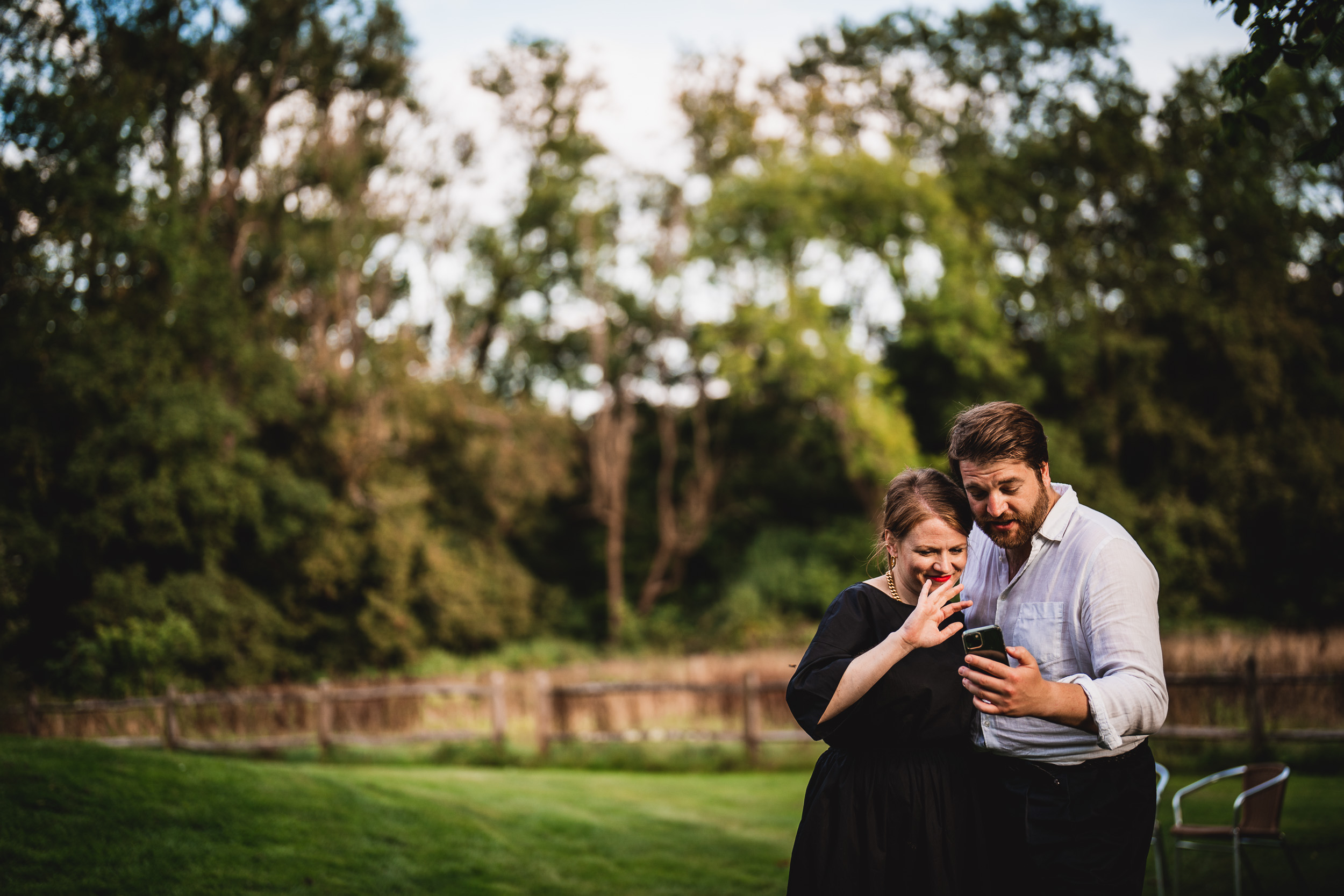 A couple looking at their cell phone in a Surrey Wedding field.
