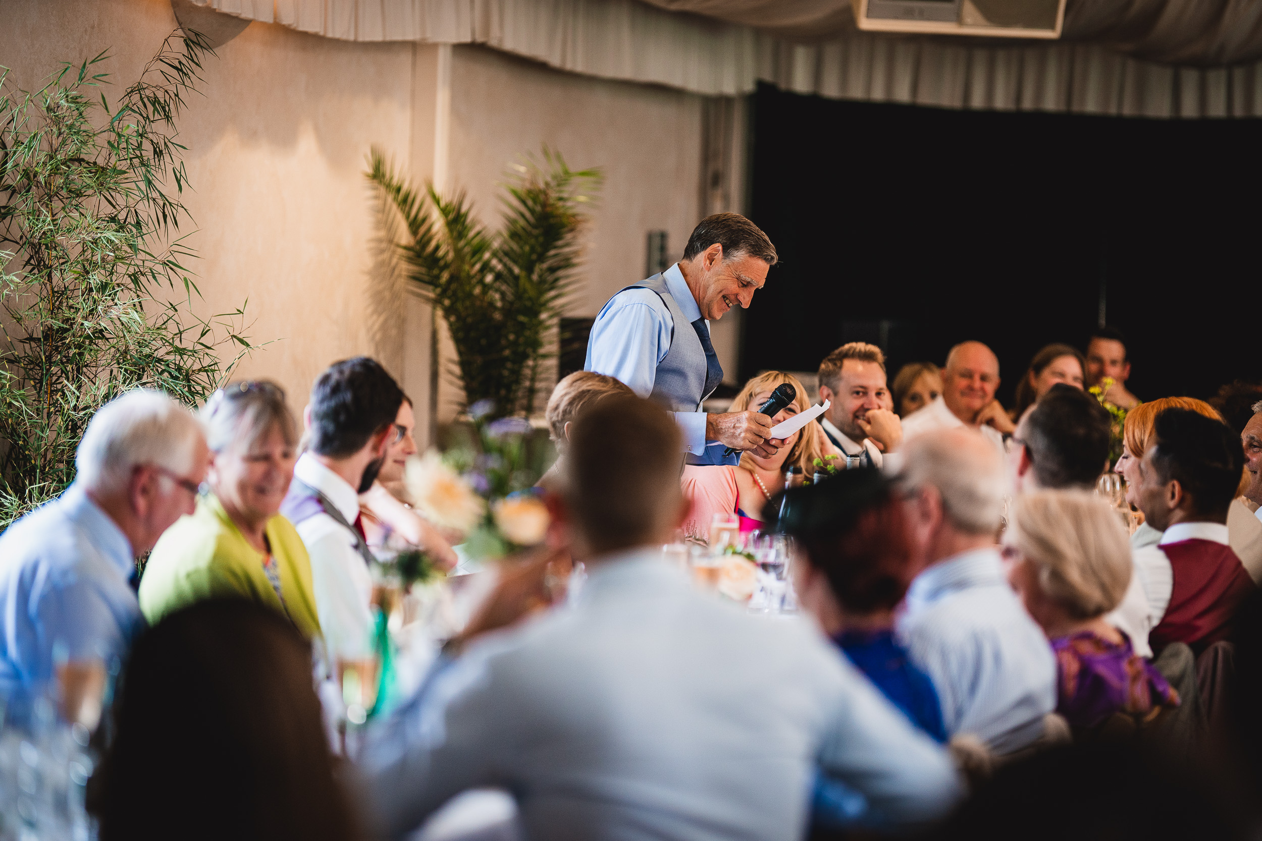 A man giving a speech to a group of people at a Surrey wedding.