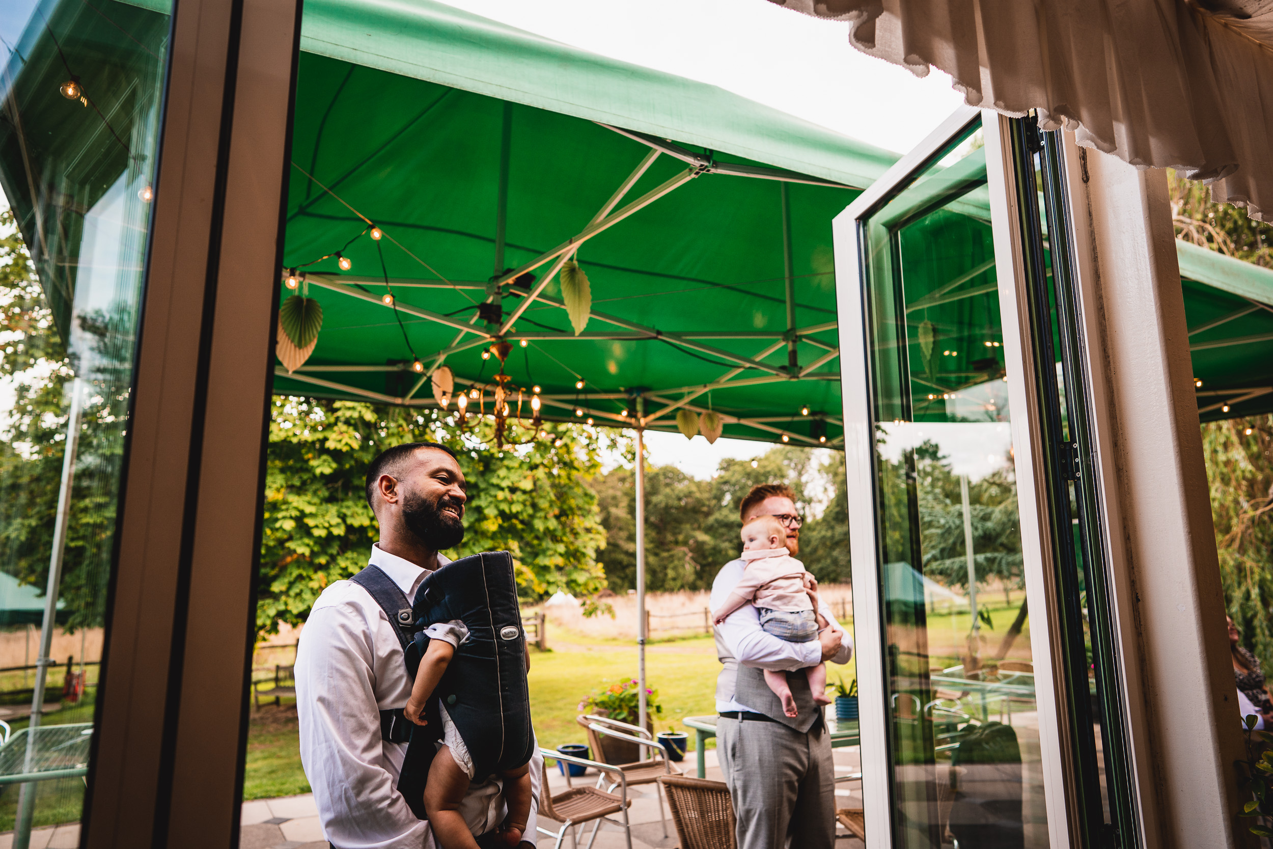 A man is holding a baby in front of a green awning at Ridge Farm.