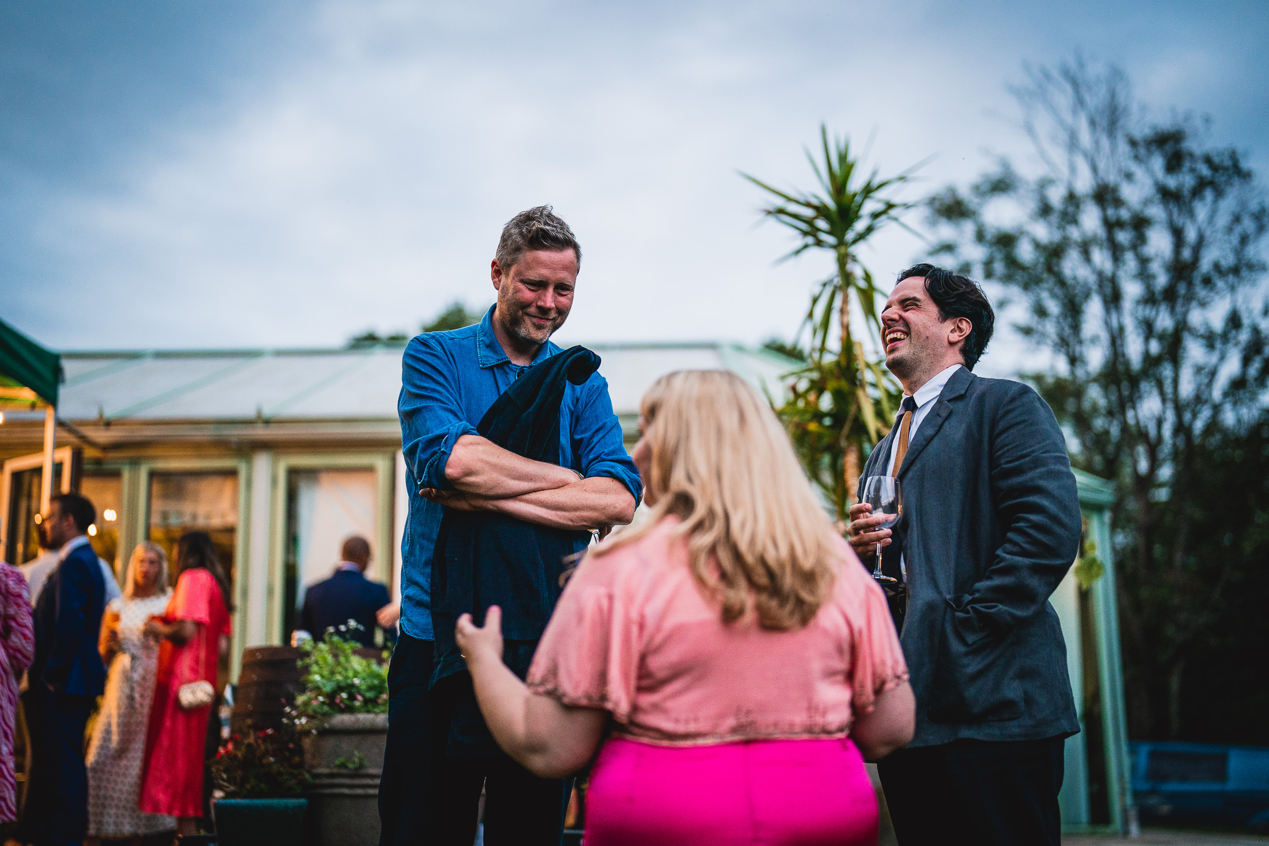 In the picturesque setting of Ridge Farm in Surrey, a group of people engage in lively conversation at a wedding reception.