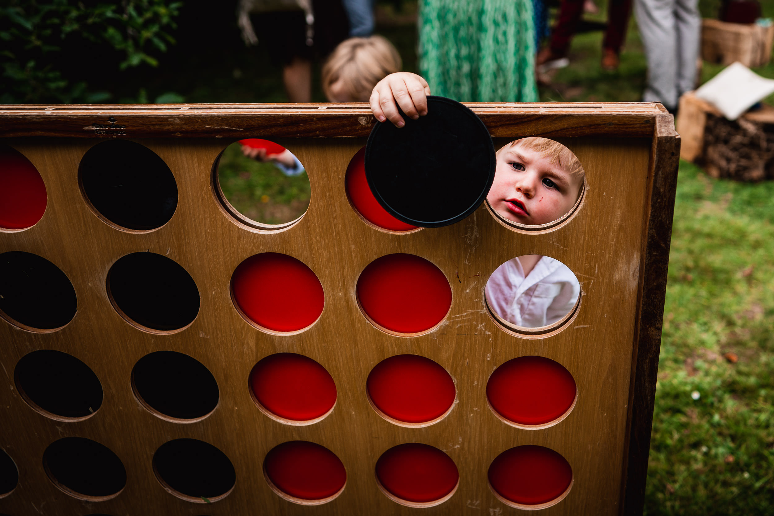 Child playing with a giant Connect Four game, holding a black disc while looking through the holes.