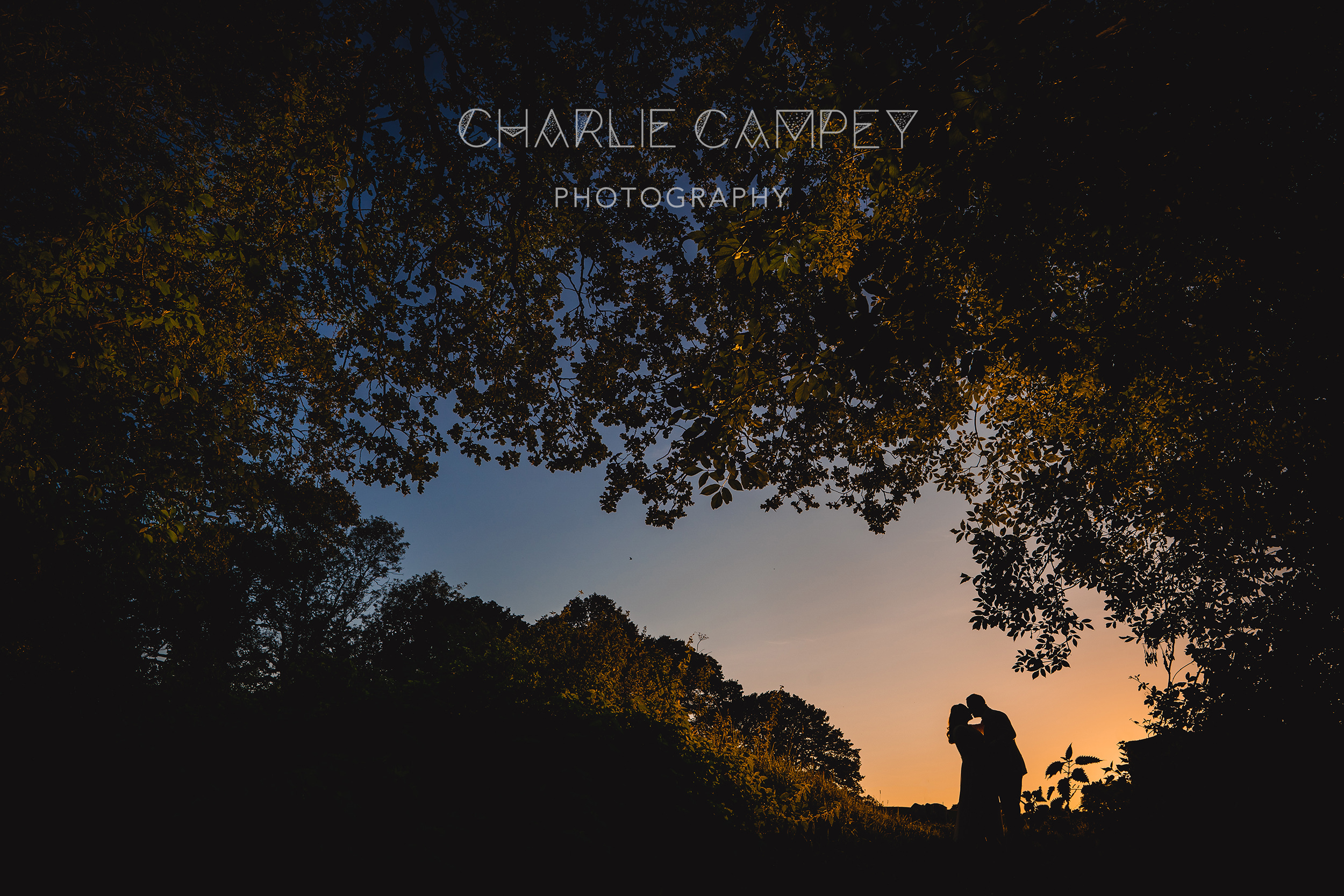 A couple embraces at sunset, silhouetted against a colorful sky and trees—a perfect moment captured for the 2025/26 Photography Brochure by Charlie Campey Photography.